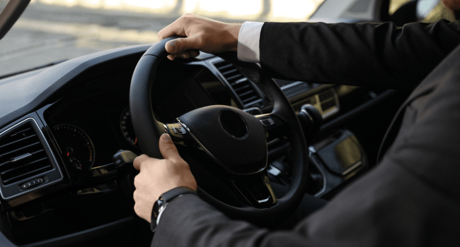 PROFESSIONAL CHAUFFEURS - Image of a well-dressed chauffeur driving a luxury limousine.